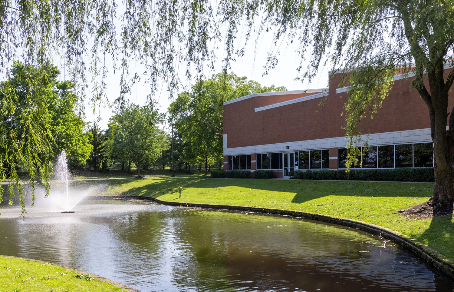 Landscaped corporate courtyard featuring pond fountain willow trees and office building at Cedar Brook