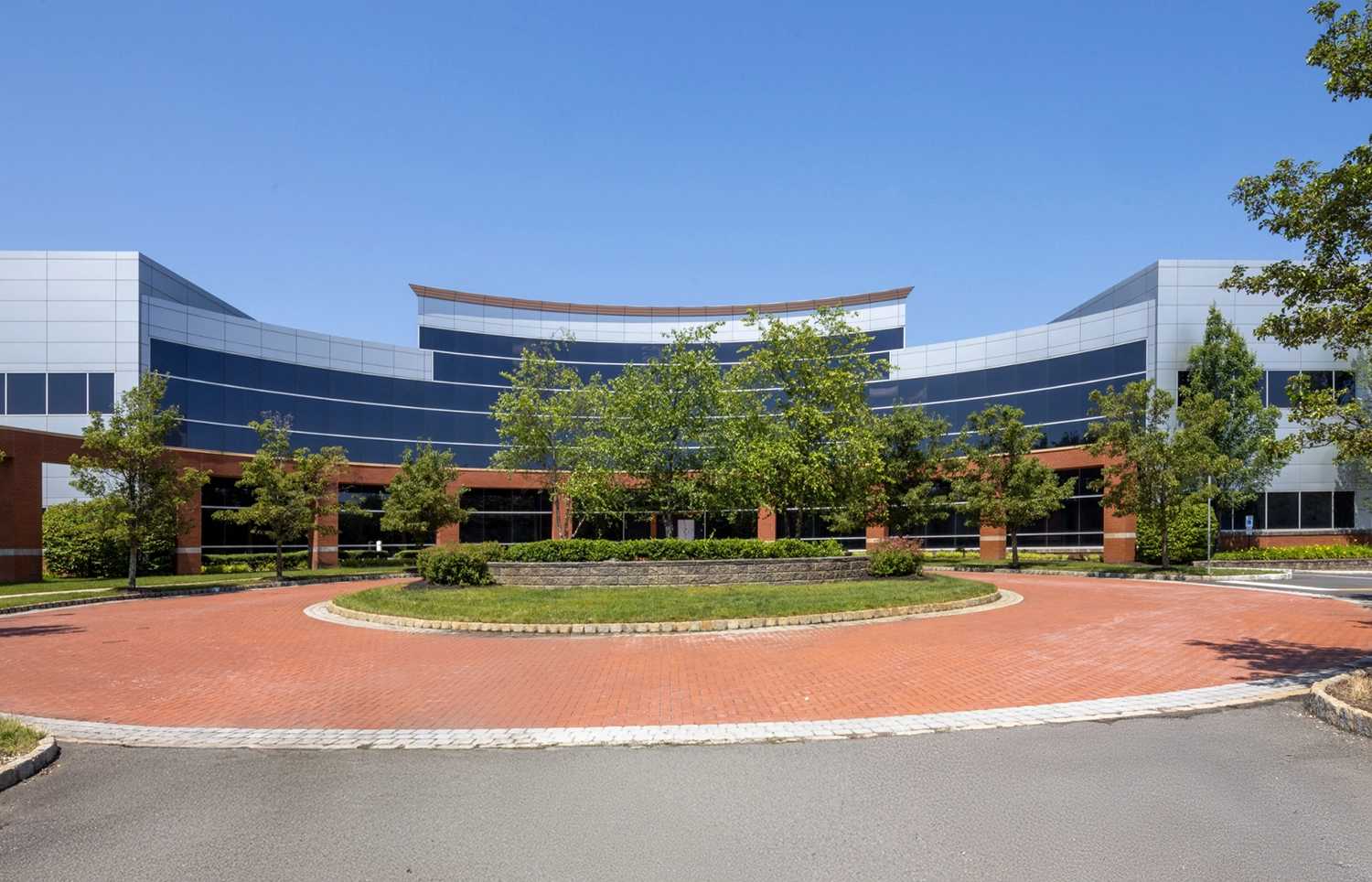 Front view of contemporary office campus with curved architecture brick driveway and greenery