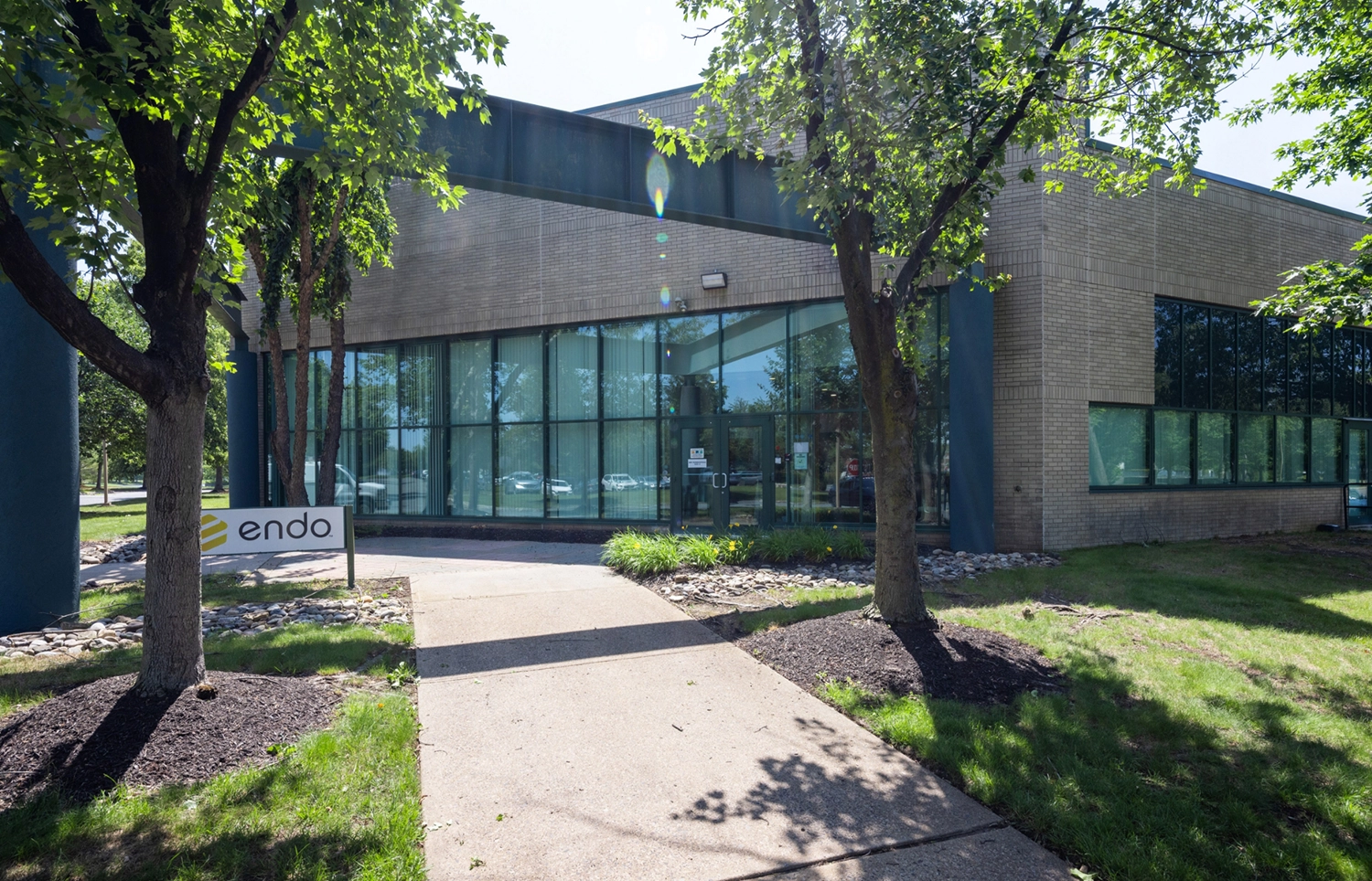 Landscaped office campus sidewalk framed by trees lawn and glass facade building