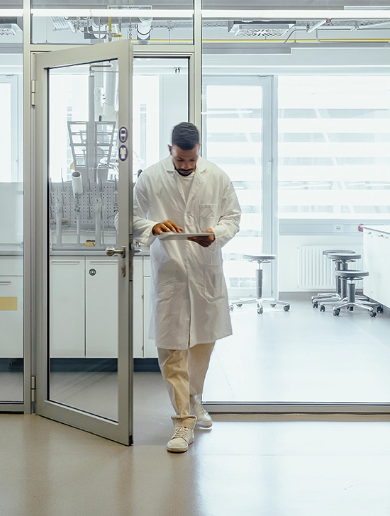 Laboratory technician in white coat reviewing data on tablet while walking through clean research facility