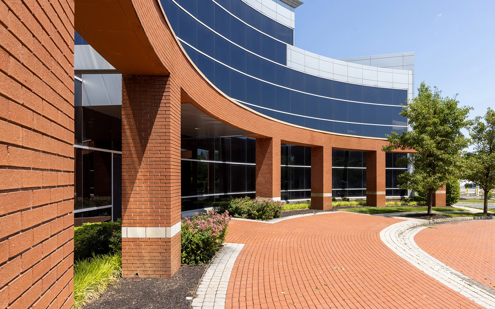 Curved glass office building with brick courtyard and landscaped green space at Cedar Brook campus