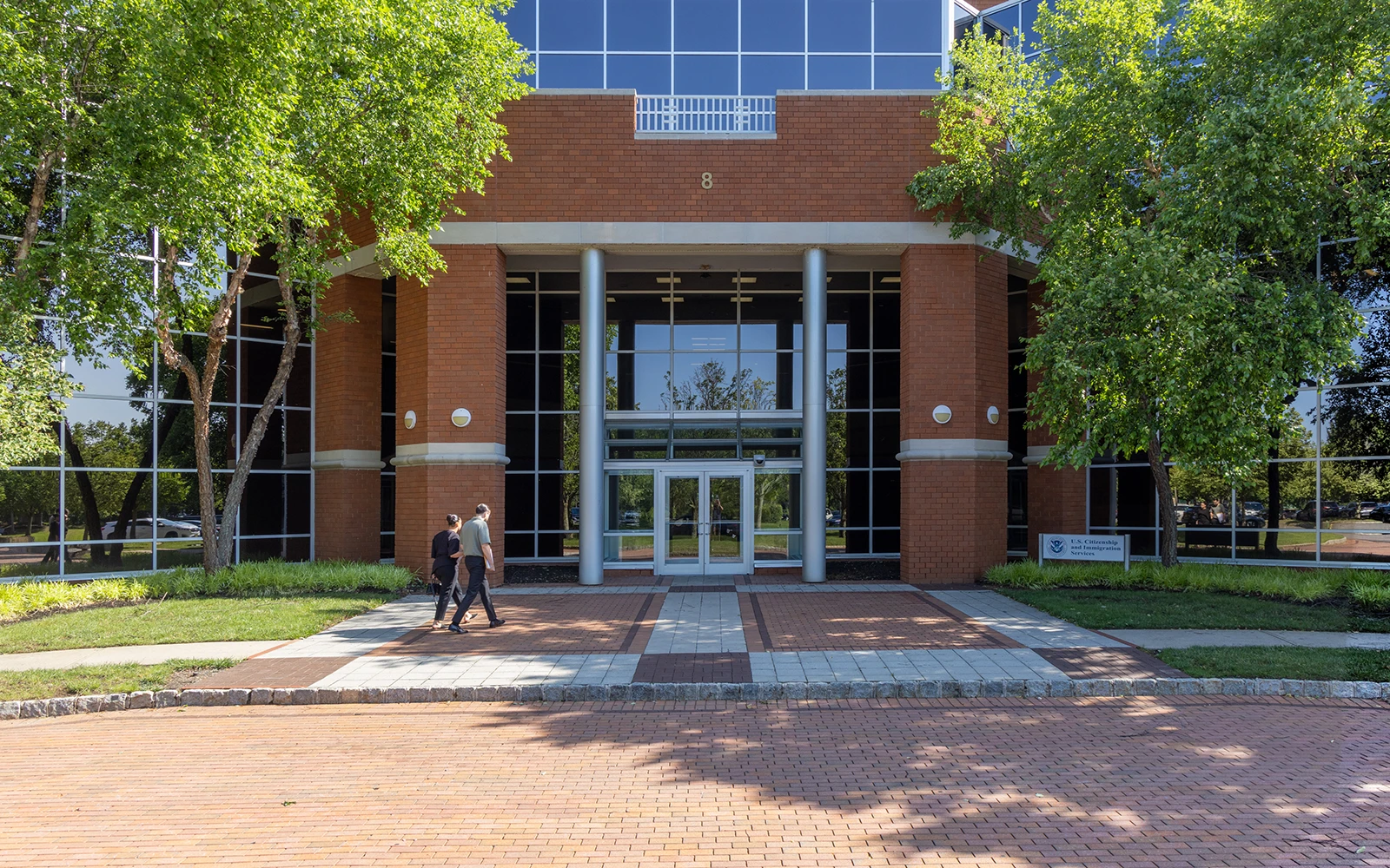 Modern office complex exterior featuring brick architecture tree lined drive and glass lobby entrance
