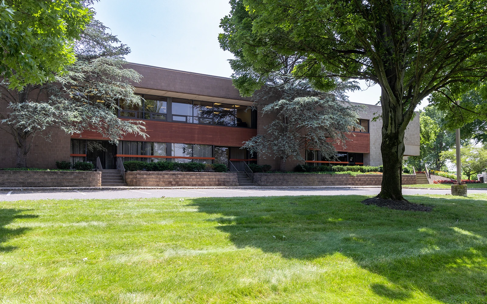 Professional business campus featuring low rise office building shaded by trees and manicured lawn