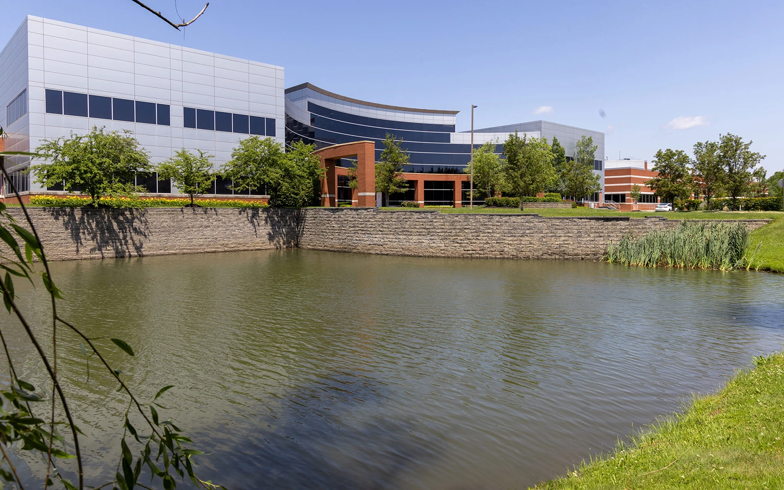 Modern glass office building beside landscaped pond and stone retaining wall at Cedar Brook