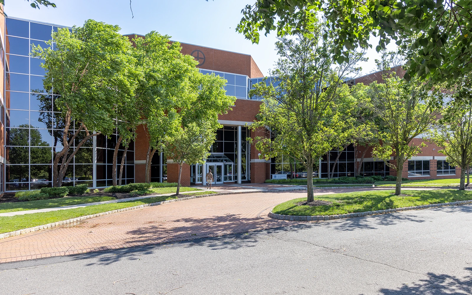 Corporate office building entrance with curved driveway mature trees glass facade and landscaped campus