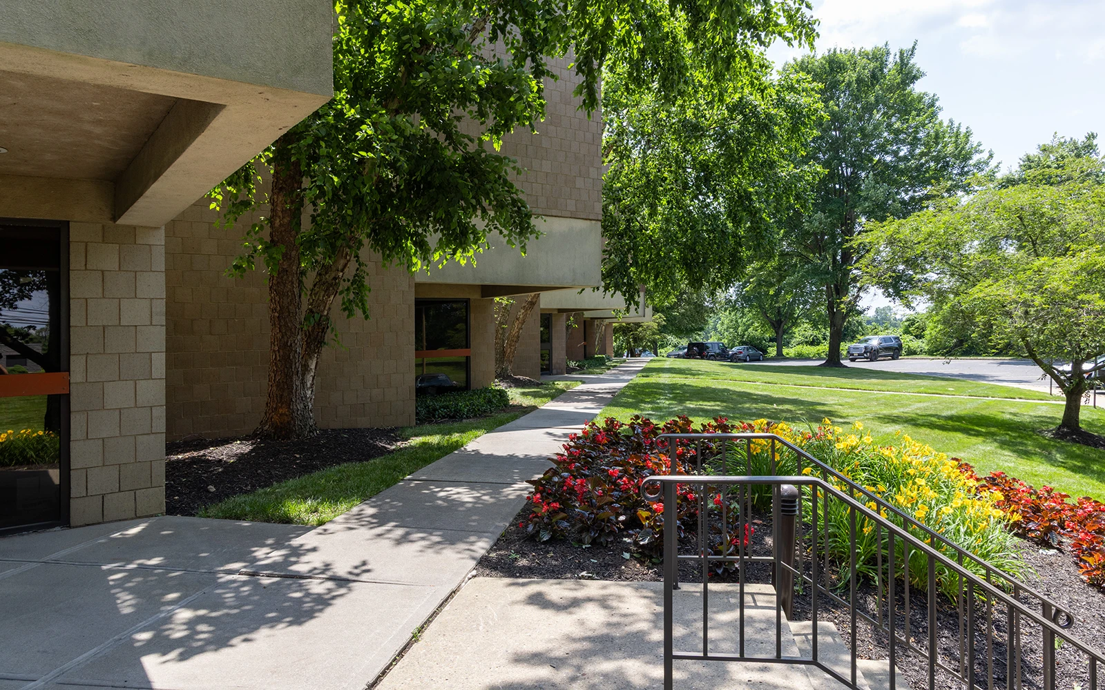 Office building exterior with landscaped walkway stairs trees and colorful flower beds on sunny day