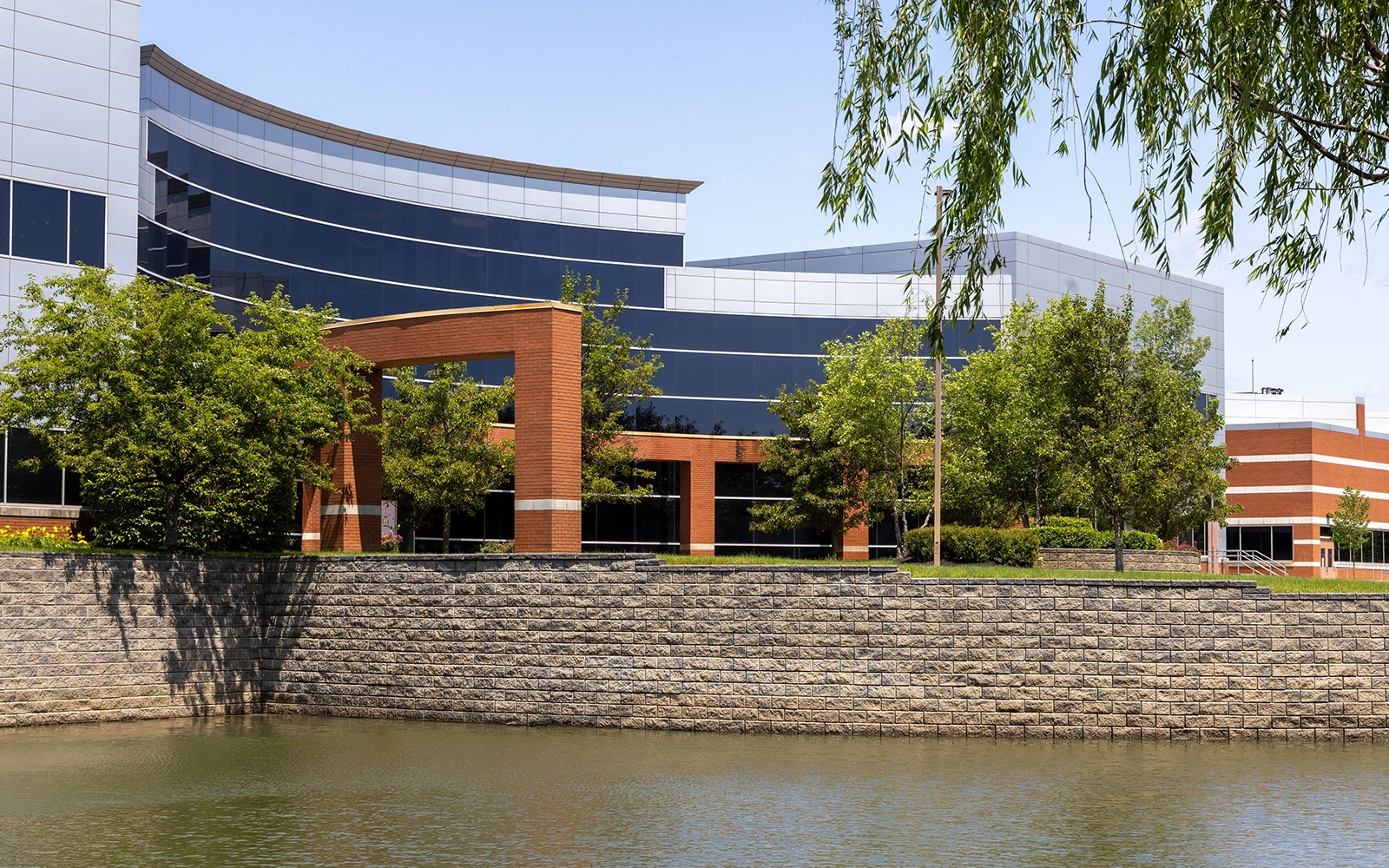 Curved corporate office exterior overlooking water feature and trees at Cedar Brook campus