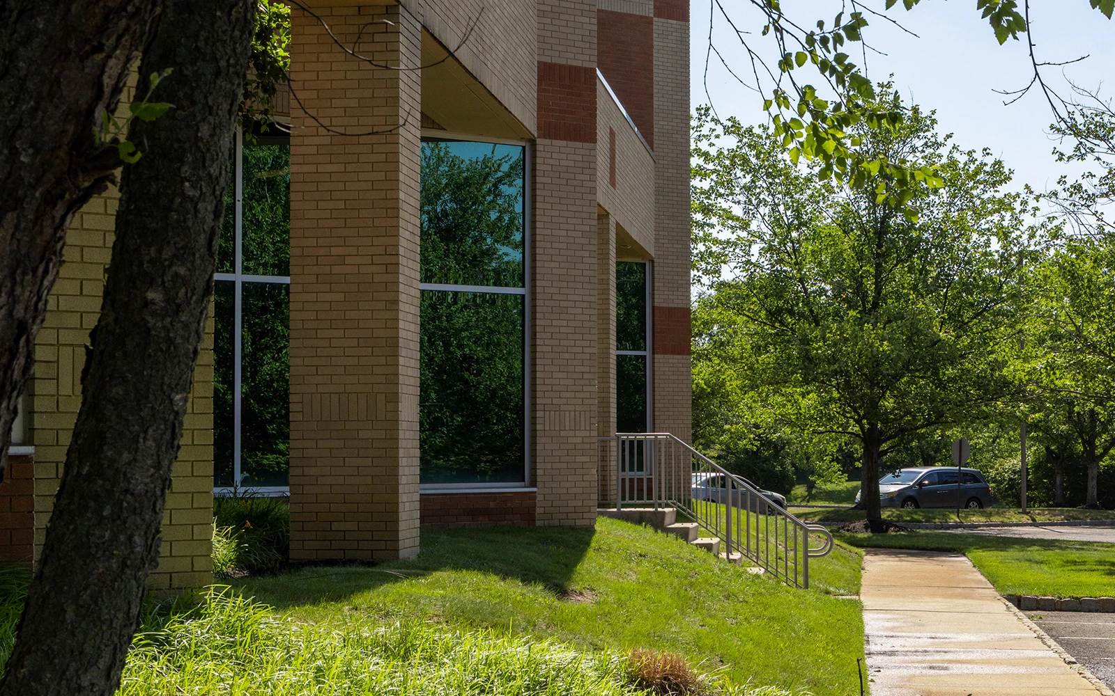 Brick office building exterior with glass windows, sidewalk, and landscaped trees at Cedar Brook campus