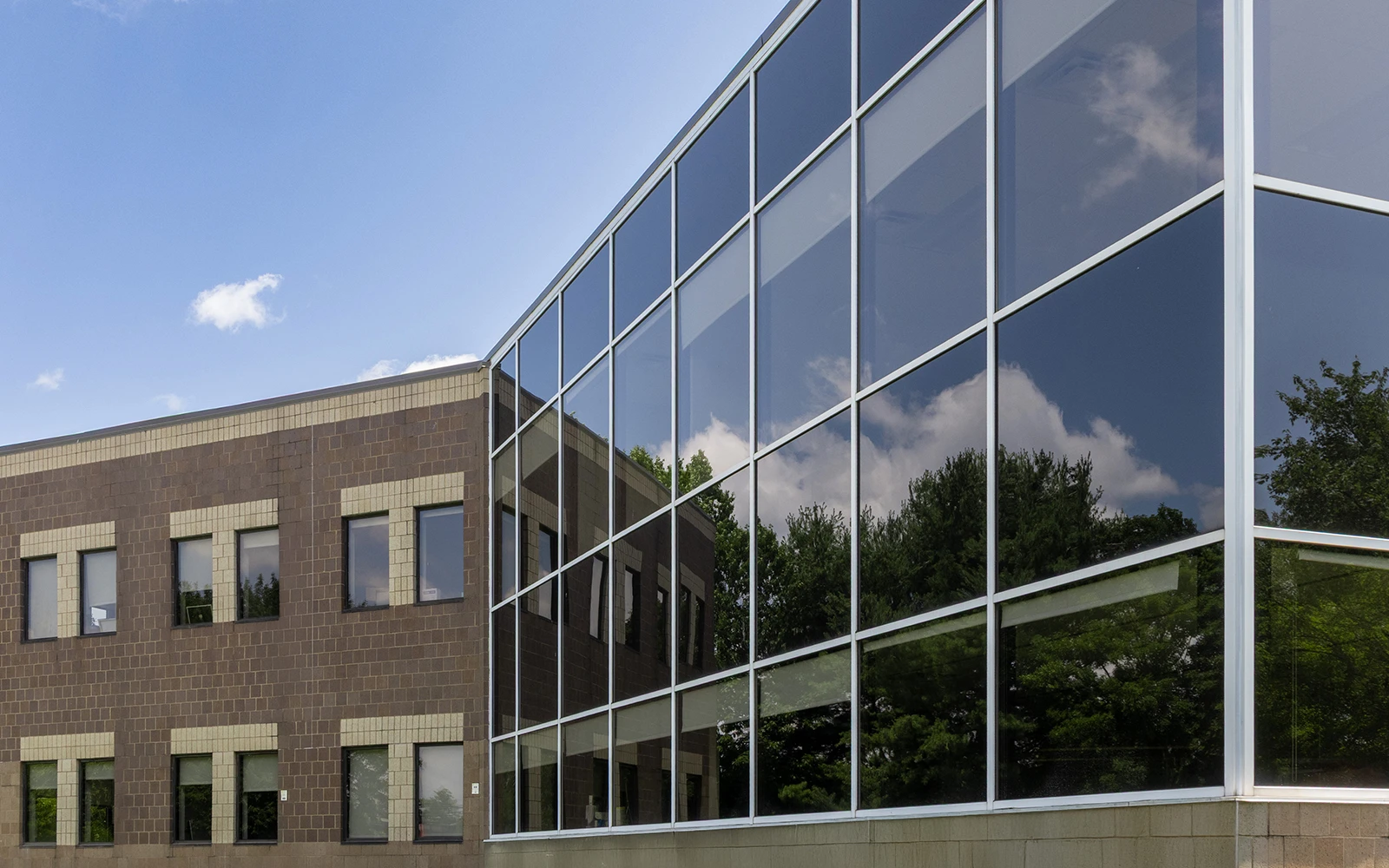 Contemporary corporate architecture featuring large glass facade reflecting trees clouds and surrounding landscape