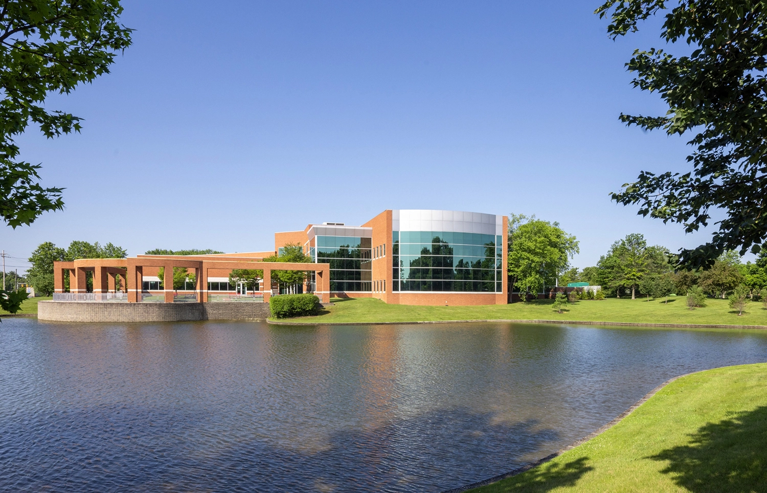 Sunlit corporate campus building with waterfront view trees and curved brick architecture