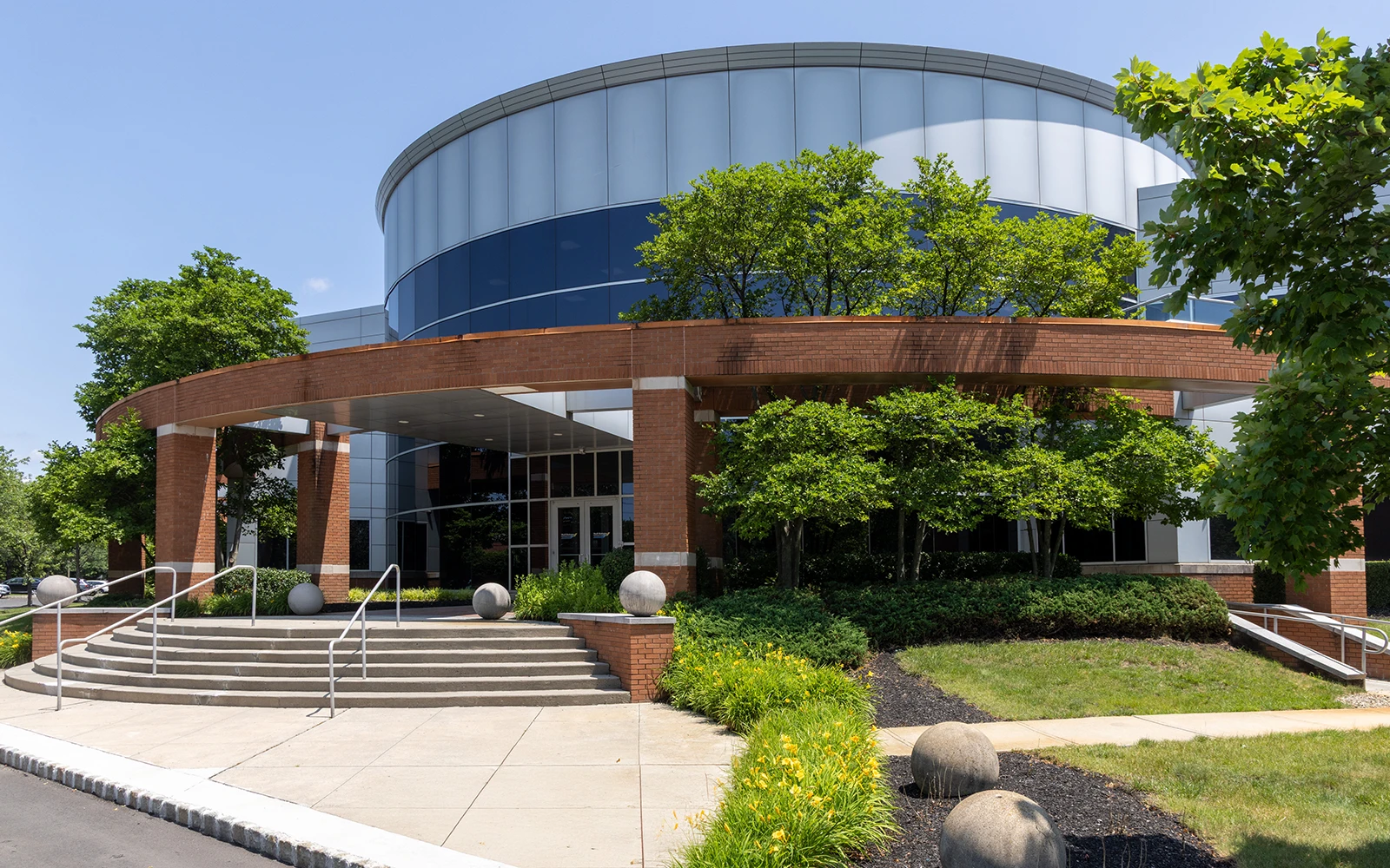 Curved glass corporate headquarters entrance with brick canopy and landscaped grounds at Cedar Brook