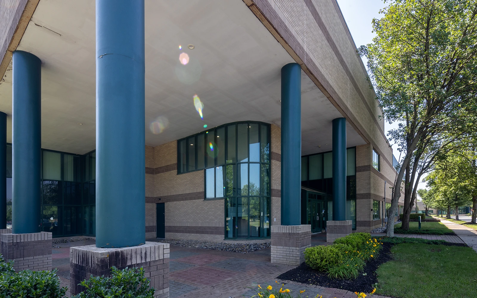 Corporate campus architecture featuring columned overhang brick facade large windows and tree lined path