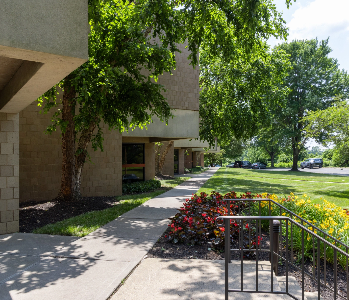 Tree shaded sidewalk and garden beds outside suburban office building at Cedar Brook
