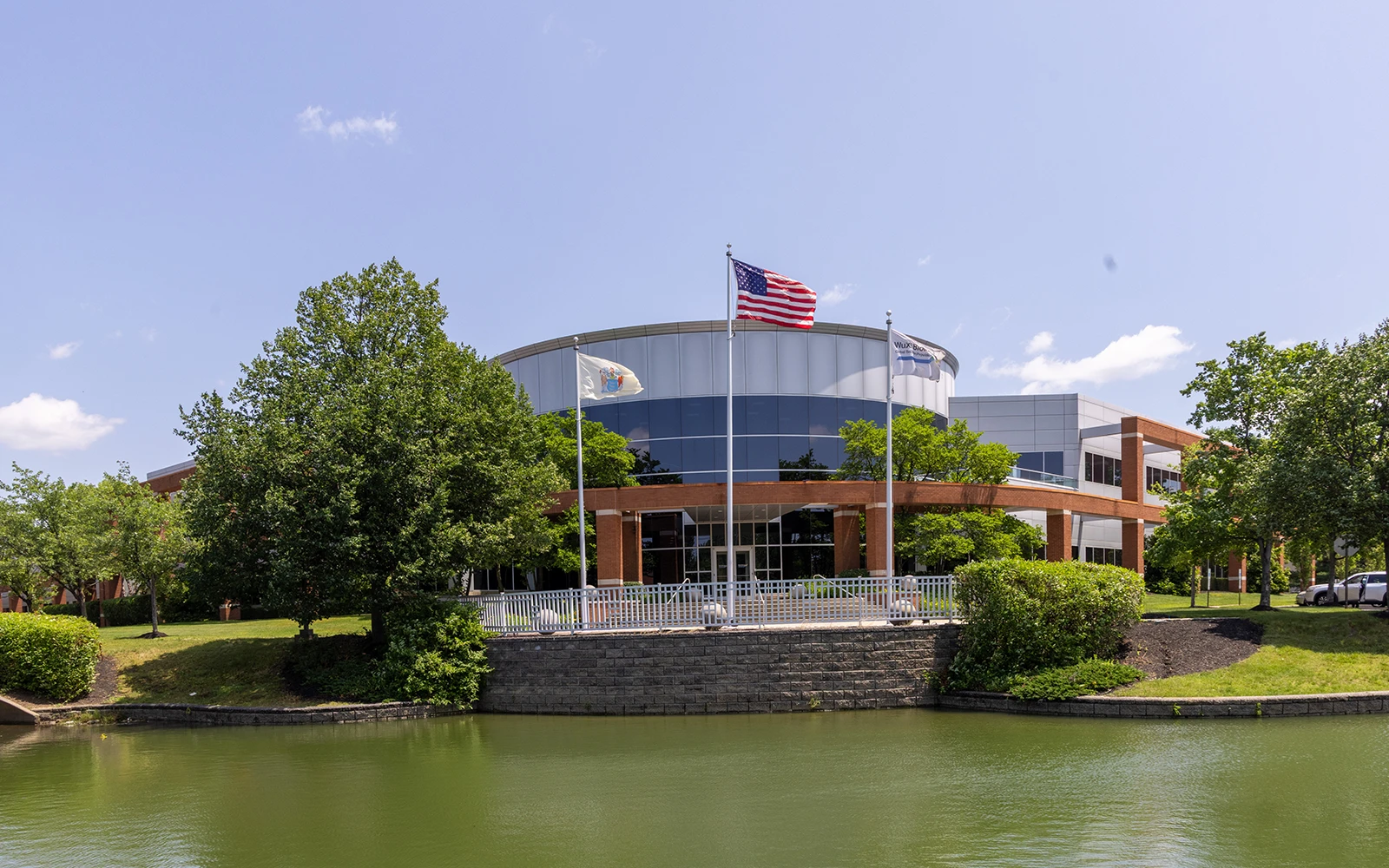 Curved glass corporate office exterior featuring flagpoles trees and brick architecture in Cranbury