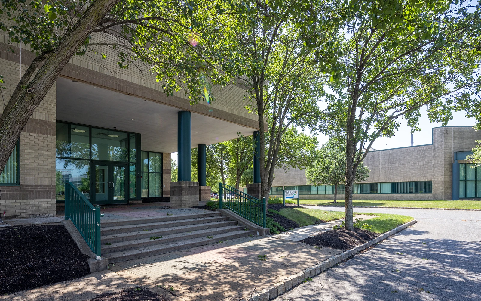 Office building entrance with covered portico stairs trees and landscaped professional campus surroundings