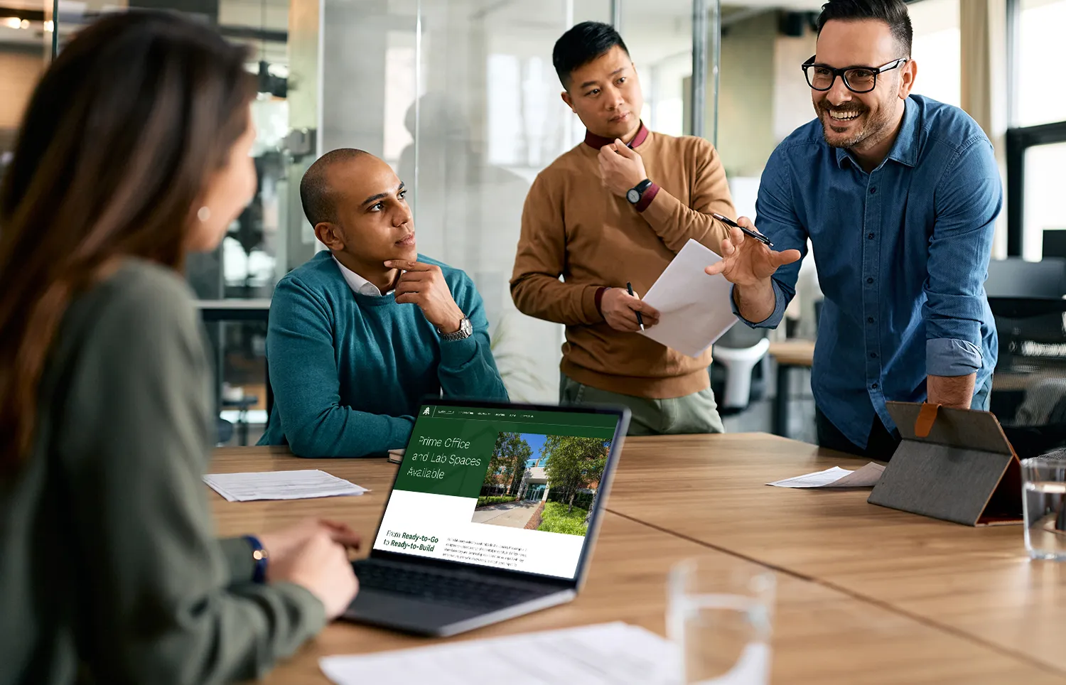 Business team collaborating in modern office meeting discussing strategy around laptop presentation